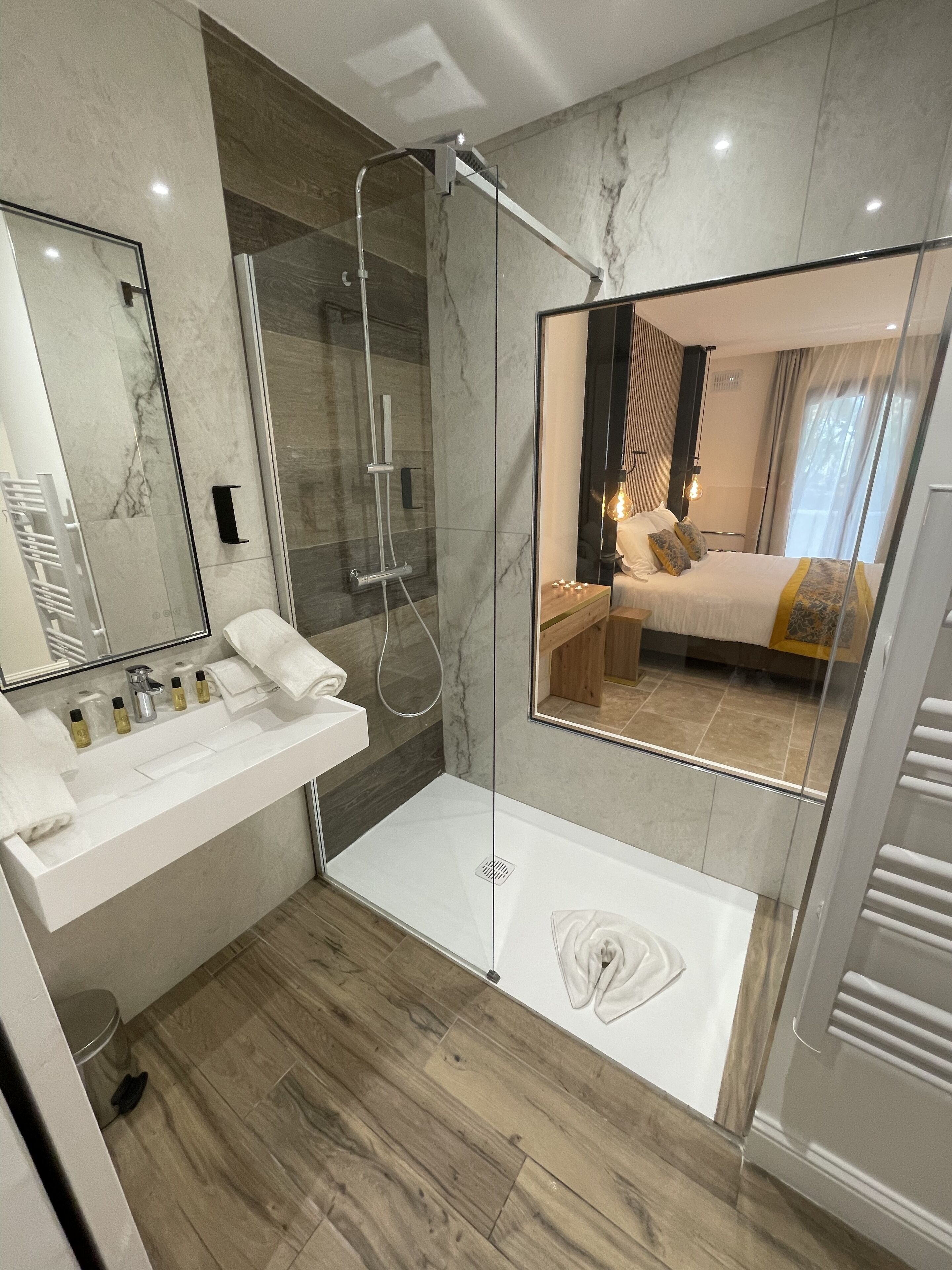 Une salle de bain moderne avec une douche à parois de verre, un lavabo blanc agrémenté d’articles de toilette et un plancher en bois.