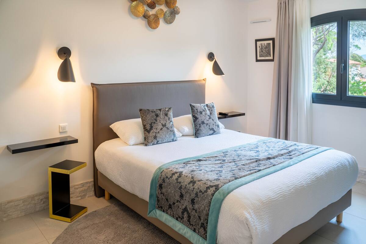 A neatly made bed with a patterned bedspread, two bedside tables with lamps, and a wall-mounted light fixture.