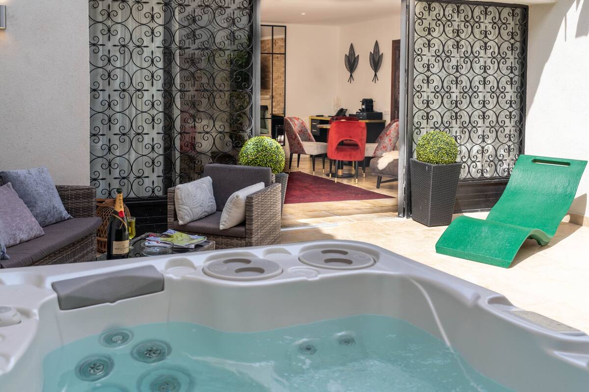 A cozy outdoor seating area with a hot tub, wicker furniture, and a dining table.