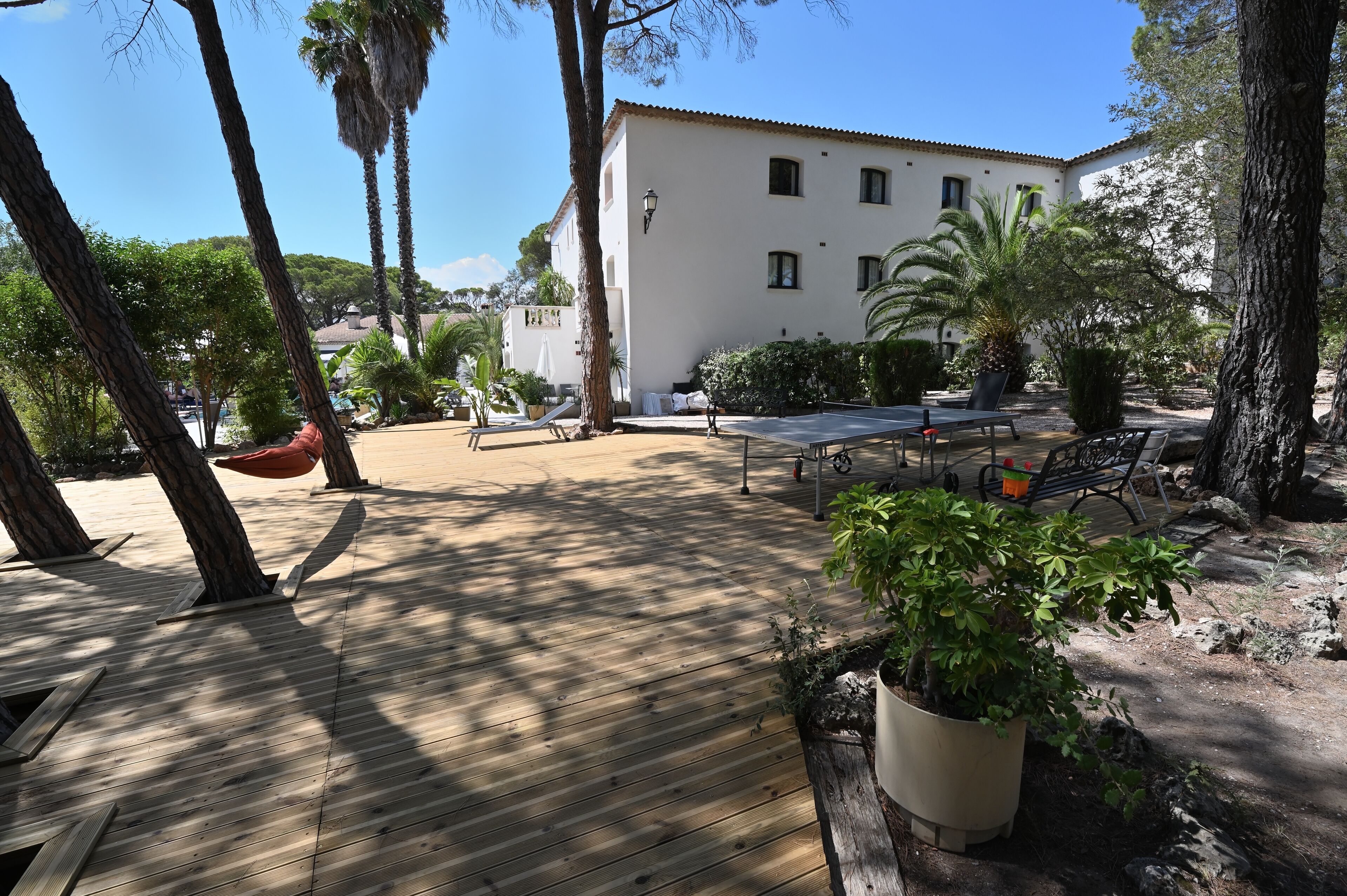 A wooden deck with outdoor furniture, a white building, and surrounding greenery.