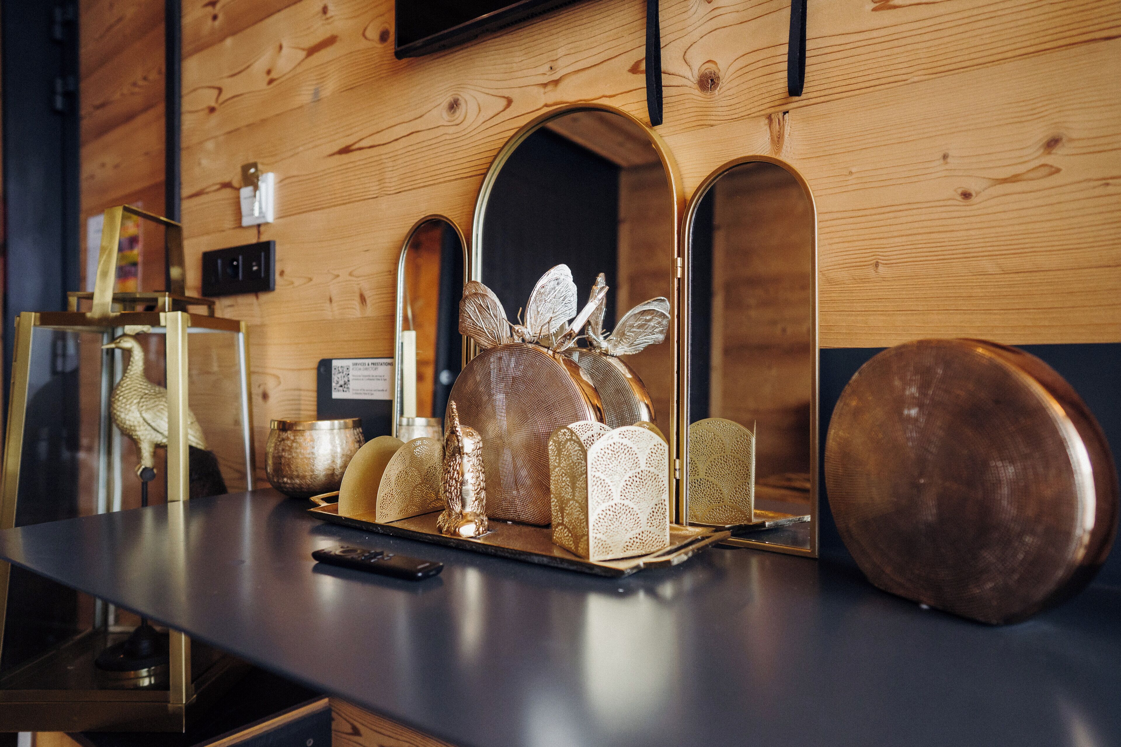 A wooden wall with a mirror and decorative items including a golden sculpture and a round wooden object.