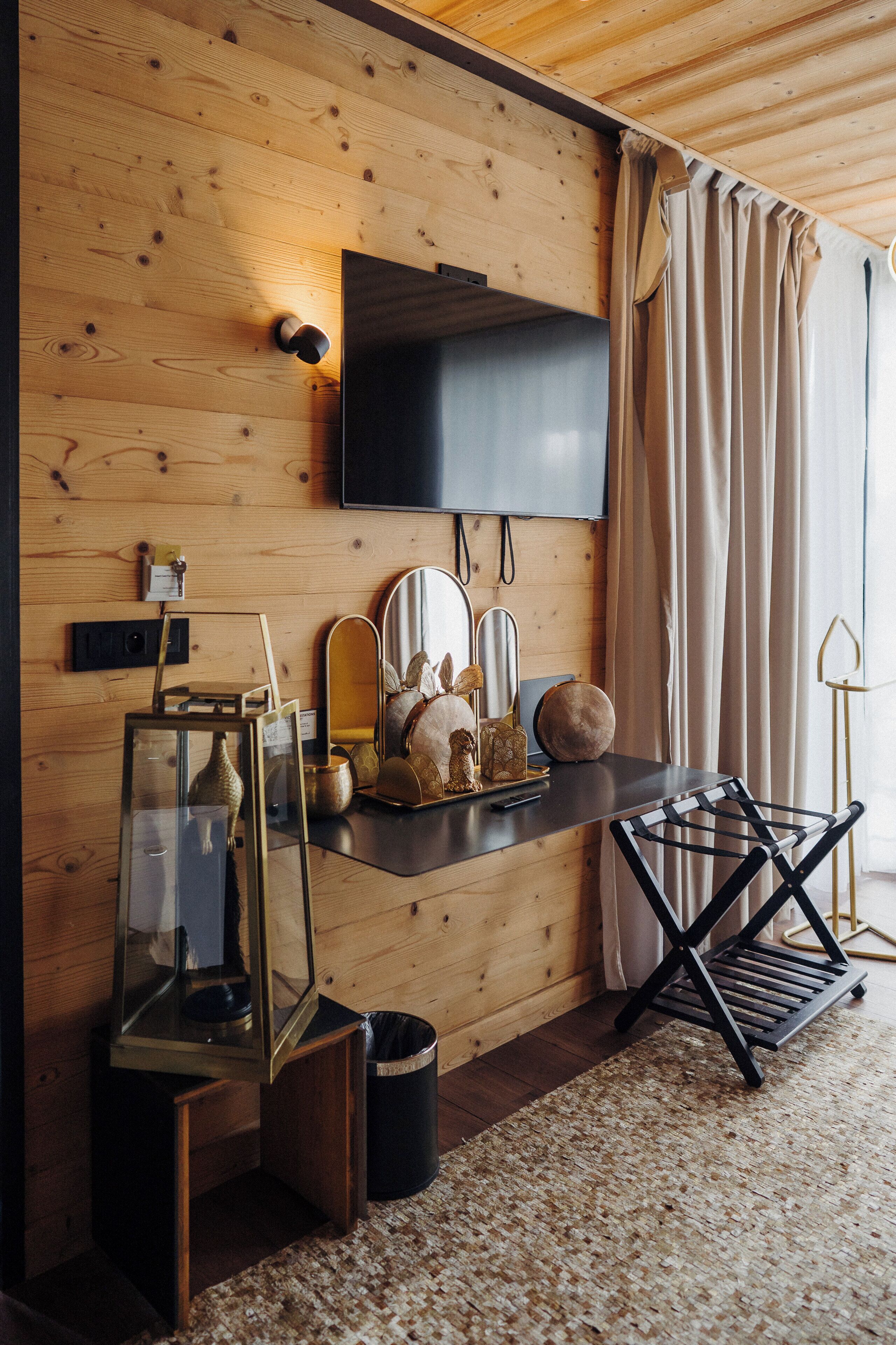 Un intérieur moderne avec un mur en bois, un téléviseur fixé au mur, une petite étagère avec des objets décoratifs, un miroir et une chaise pliante noire.