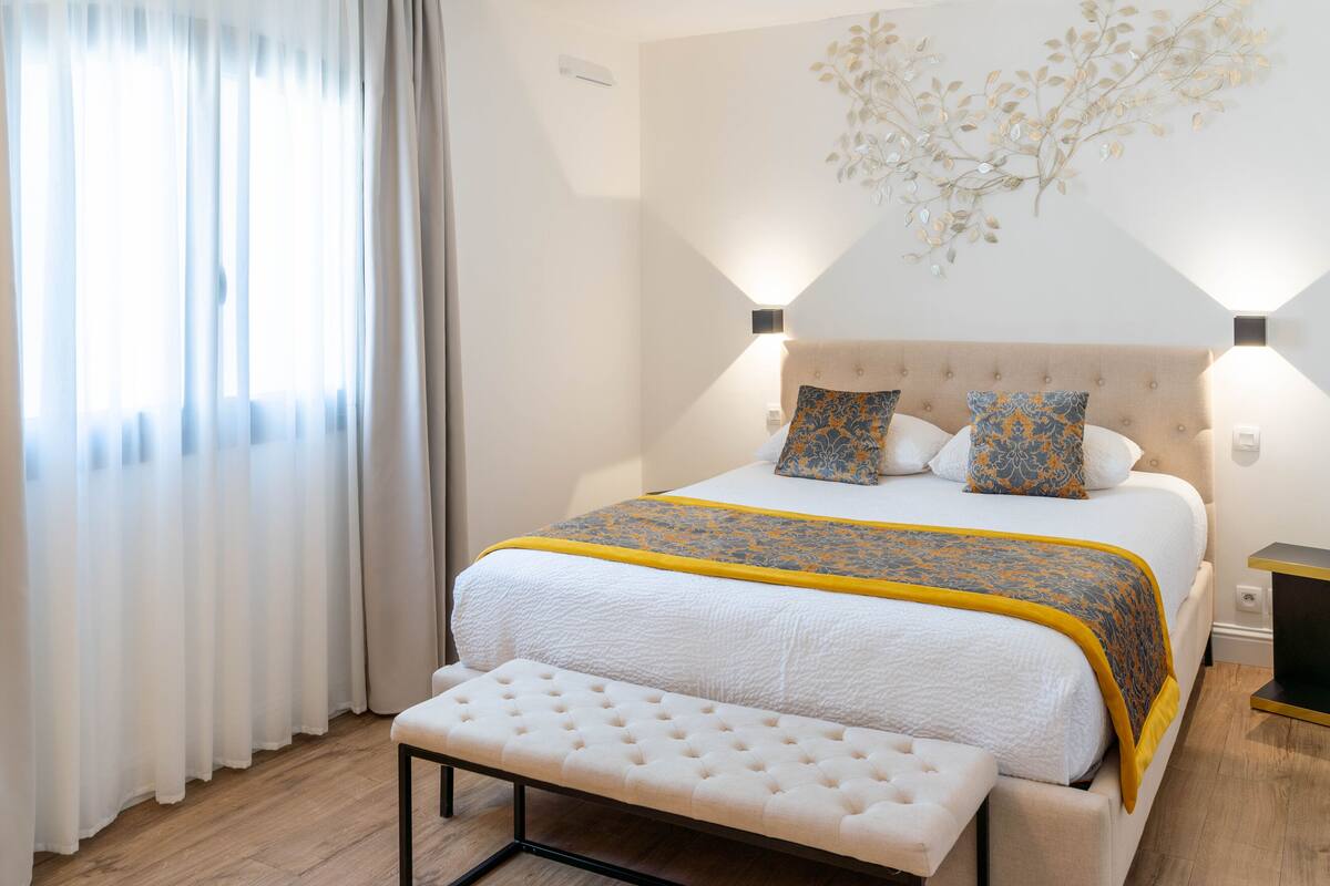 A neatly arranged bedroom with a bed, bench, and wall-mounted lights.
