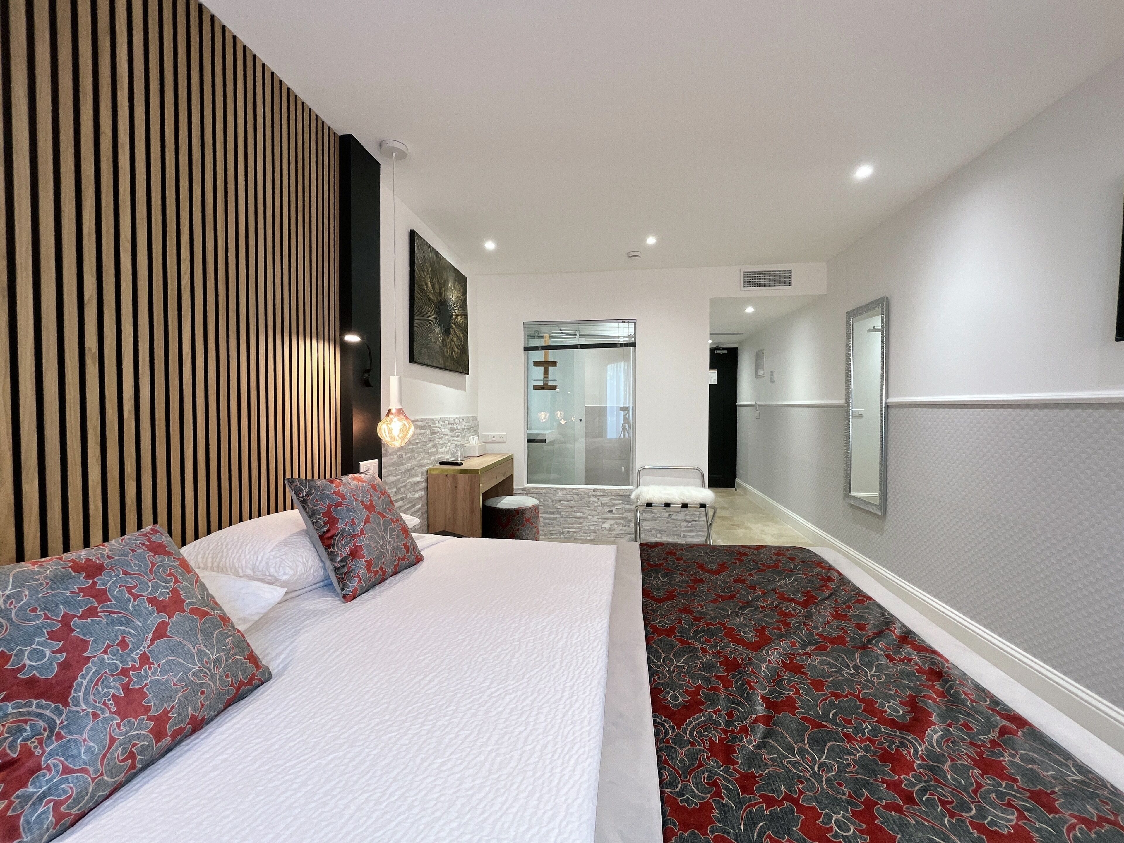 A modern hotel room with a large bed, a desk, and a bathroom visible through a glass door.