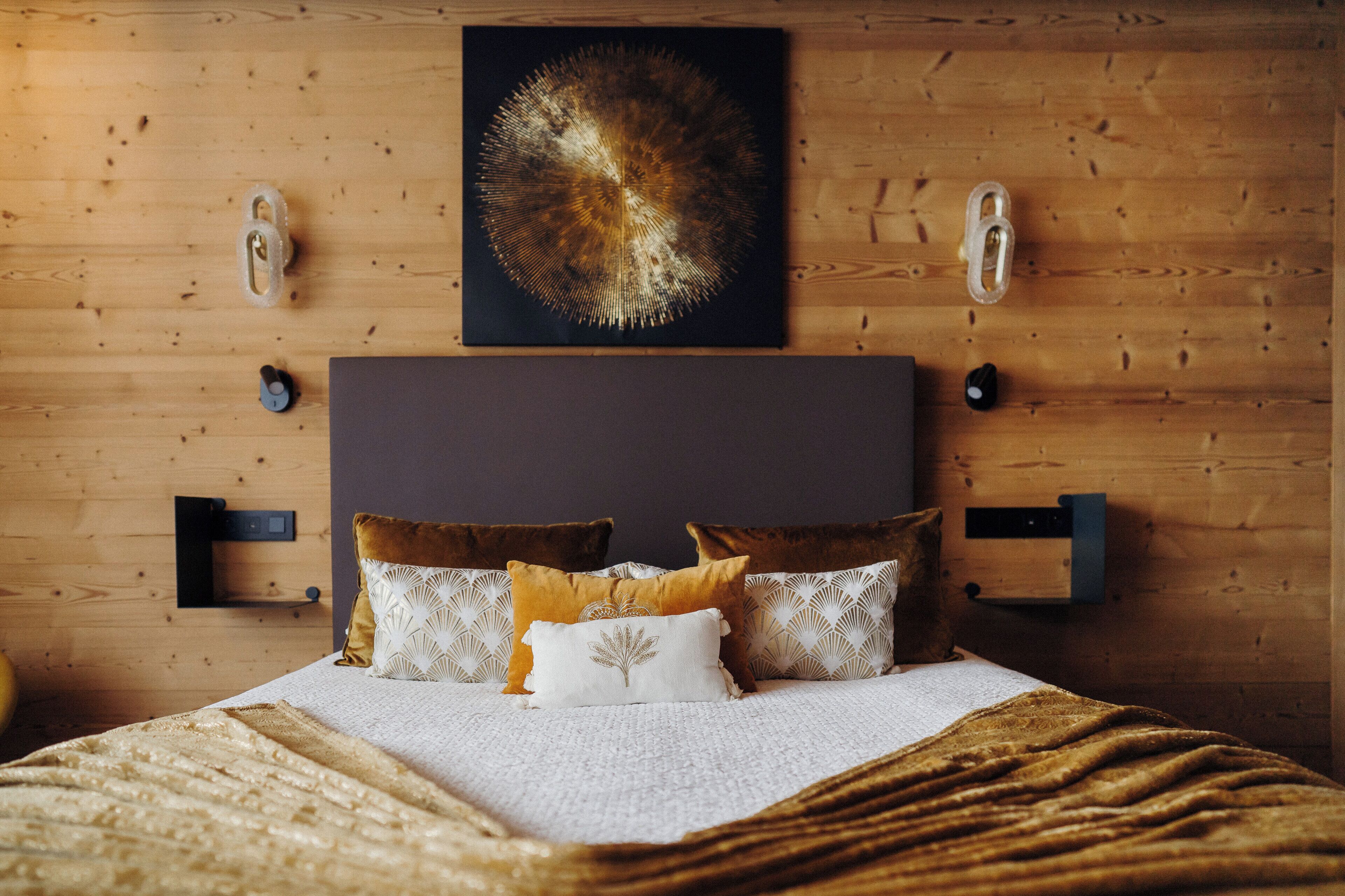 A bedroom with a wooden headboard, a bed with multiple pillows, and a wall-mounted artwork.