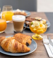 Un desayuno con cruasanes, un vaso de zumo de naranja, una taza de café y un bol de fruta.