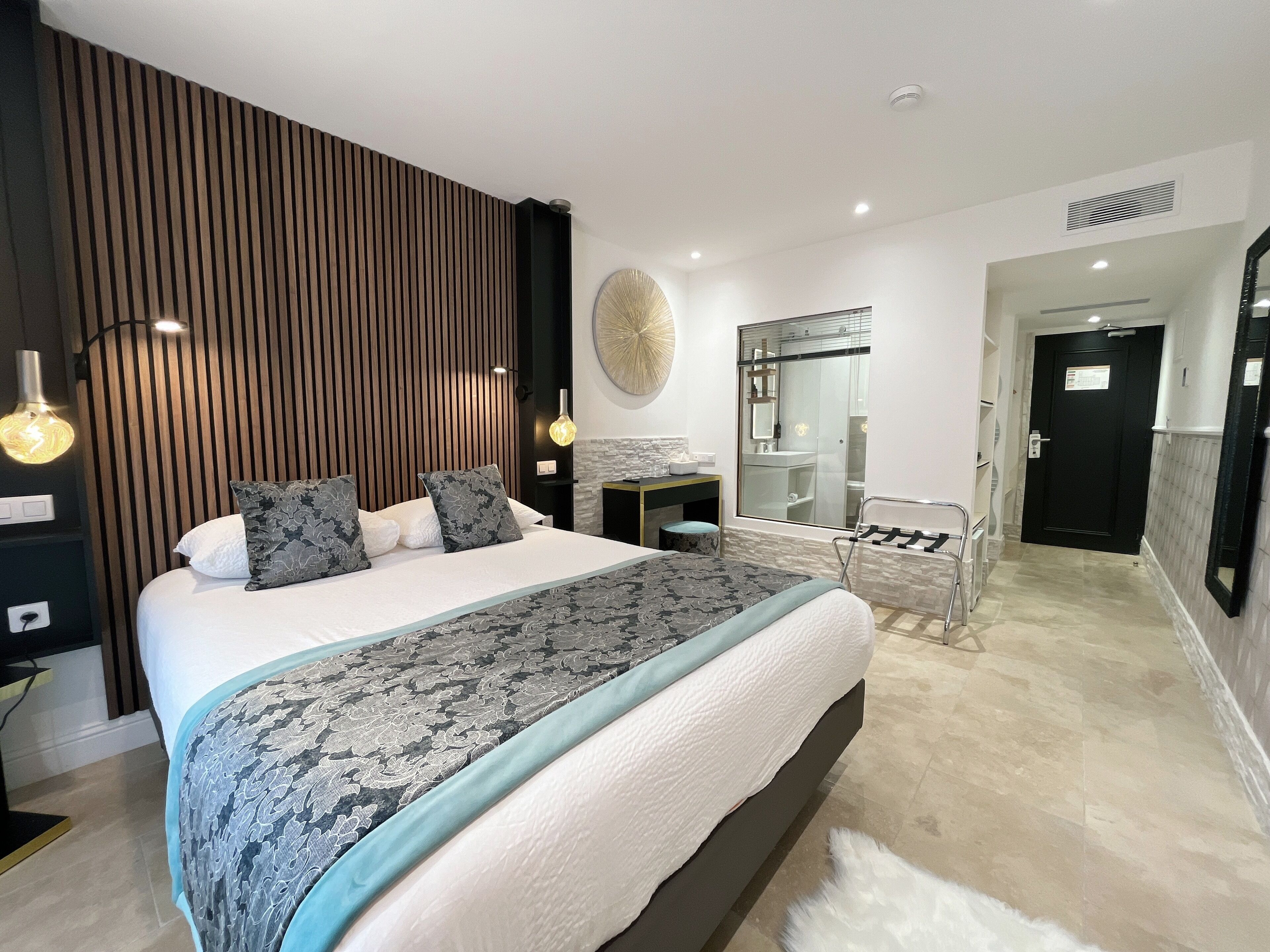 A modern bedroom with a large bed, bedside tables, a mirror, and a view of the bathroom.