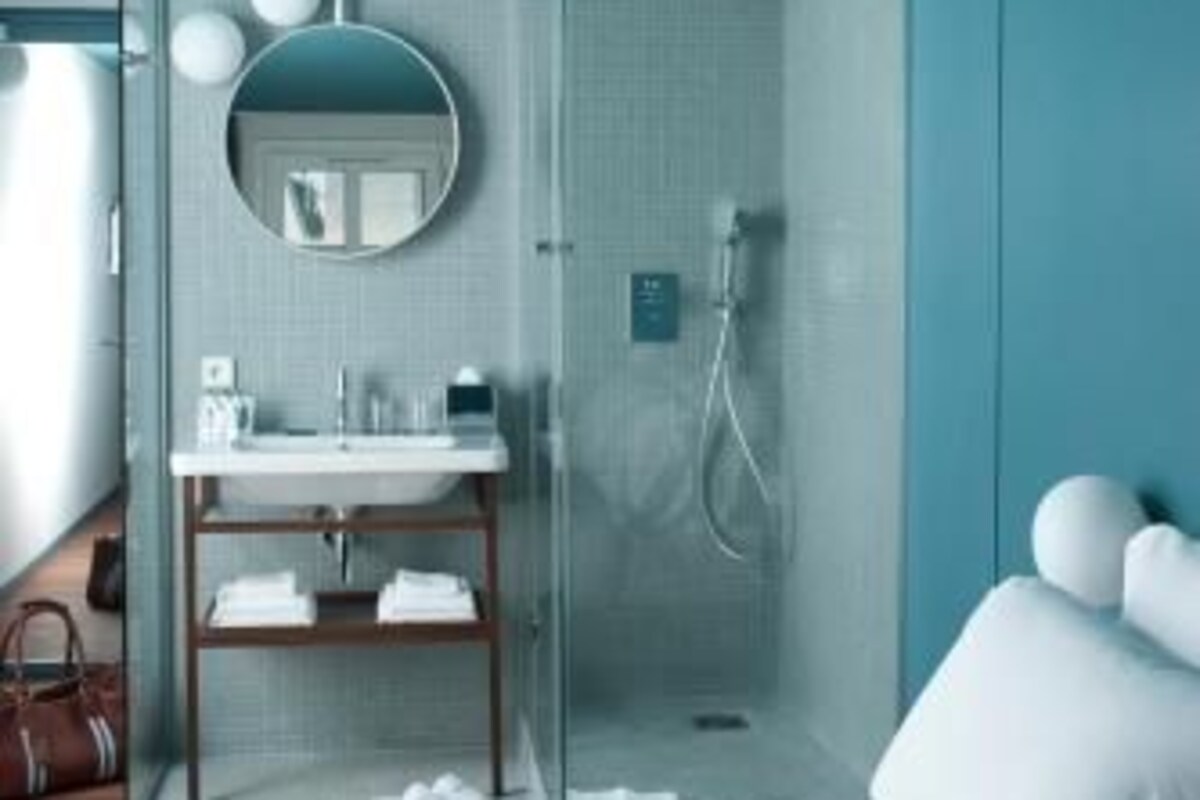 A modern hotel room with a bed, a bathroom with a shower, and a round mirror.