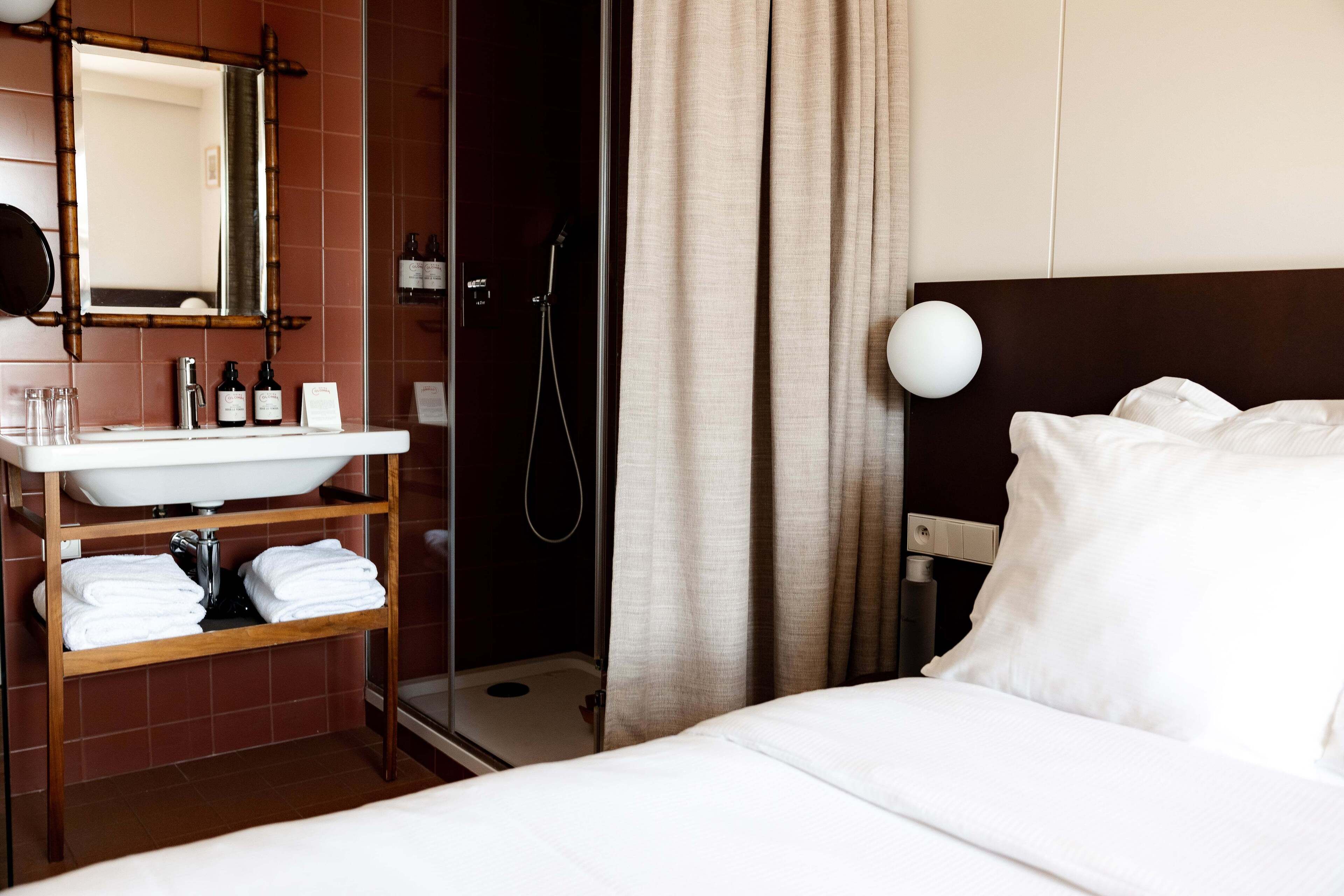A hotel room with a bed, a bathroom with a sink, and a shower.