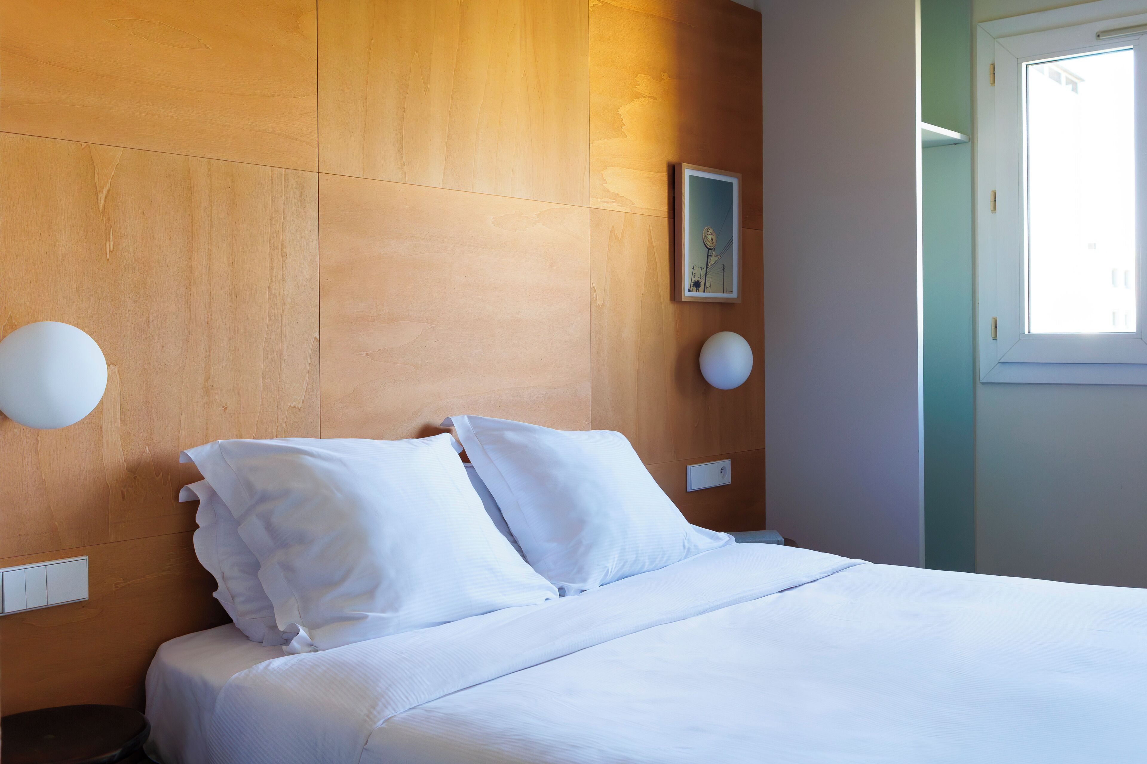 A neatly made bed with white linens in a room with wooden paneling and a window.