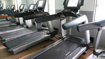 A row of treadmills in a gym with a mirrored wall and a door in the background.