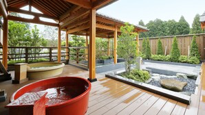 A wooden deck with a covered area, a hot tub, and a landscaped garden with rocks and plants.