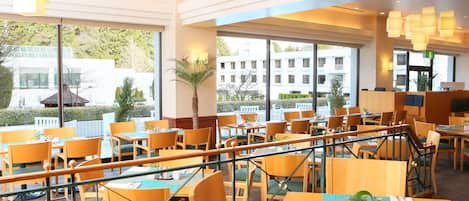 A spacious restaurant with multiple tables and chairs, large windows offering a view of the outside, and a modern interior design.
