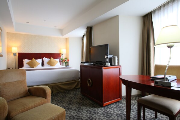 Una habitación de hotel con una cama, un escritorio, una silla, un televisor y una lámpara.
