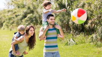 A family with two children on a grassy field, one child on a man's shoulders, and a beach ball in the air.