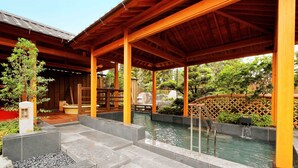 A covered outdoor area with a stone pathway leading to a water feature, surrounded by wooden structures and greenery.