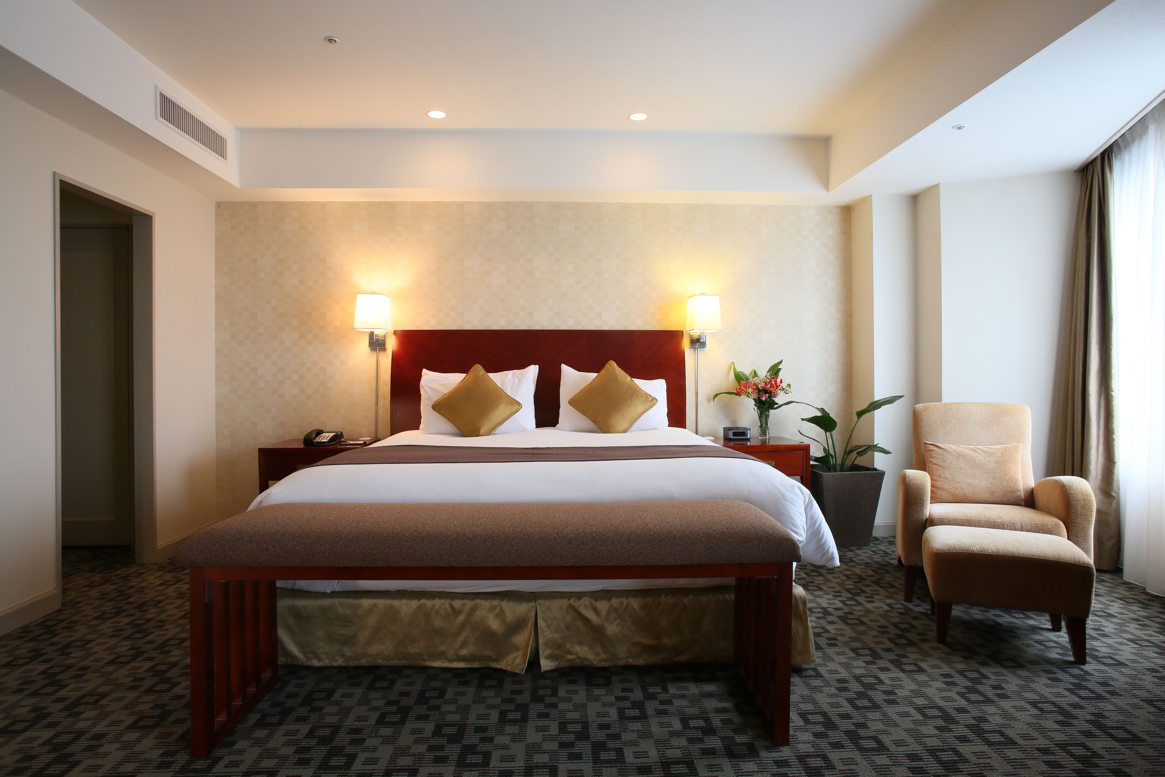 A hotel room with a large bed, two bedside lamps, a chair, and a potted plant.