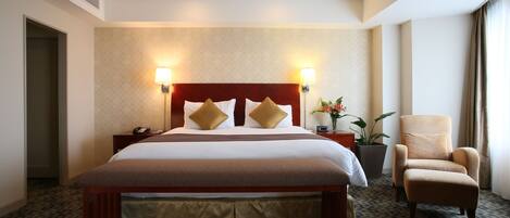 A hotel room with a large bed, two bedside lamps, a chair, and a potted plant.