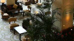 A spacious lounge area with comfortable seating, large windows offering a view of a well-manicured garden, and a prominent pillar with the name "Vista Lounge".