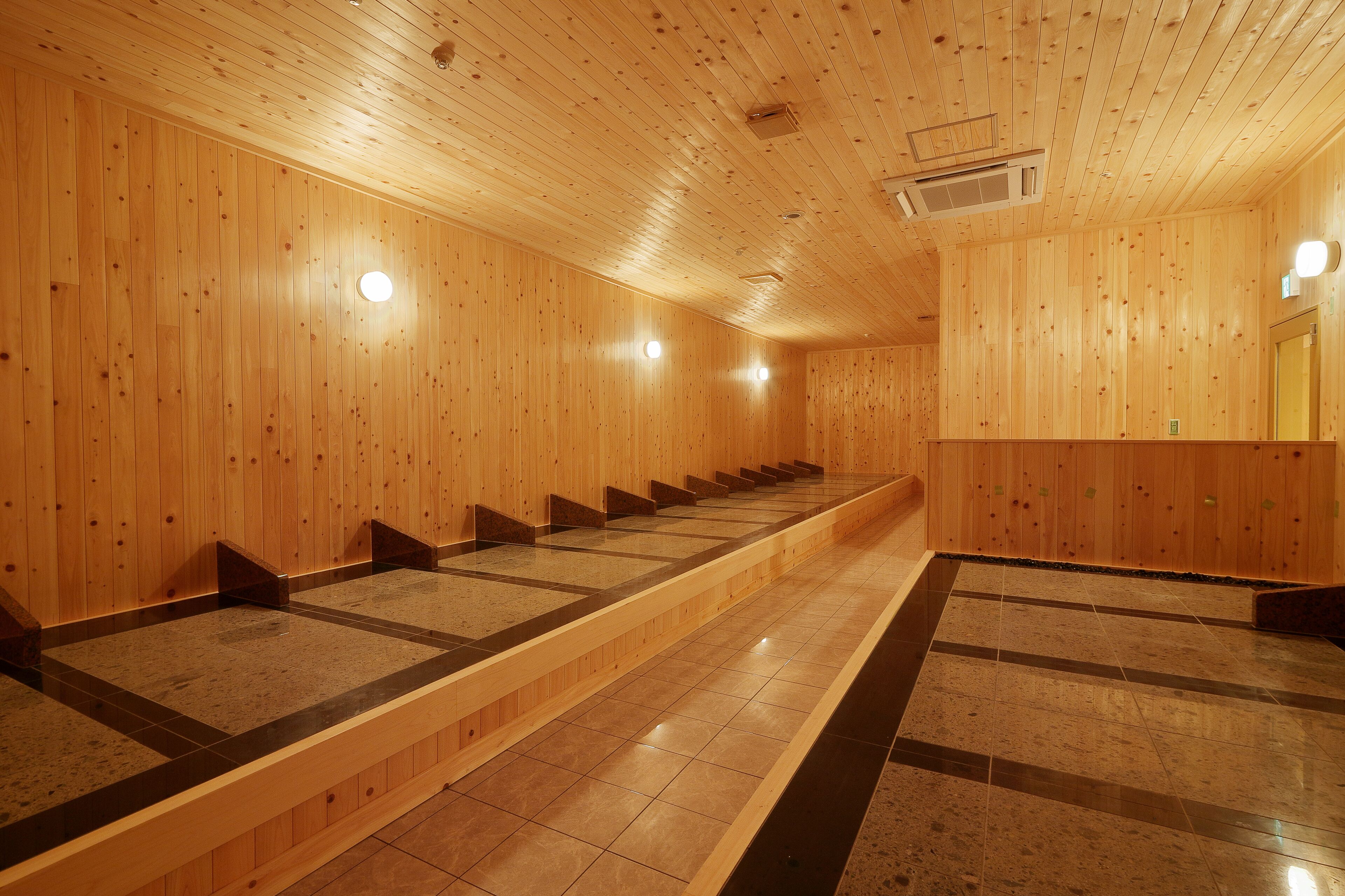 Una sauna con paredes y bancos de madera, suelo de baldosas y techo con ventilación.