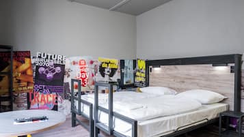 A modern room with a bunk bed, a round table with a remote control, and posters on the wall advertising events.