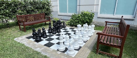 Un tablero de ajedrez a cuadros dispuesto al aire libre, con bancos alrededor.
