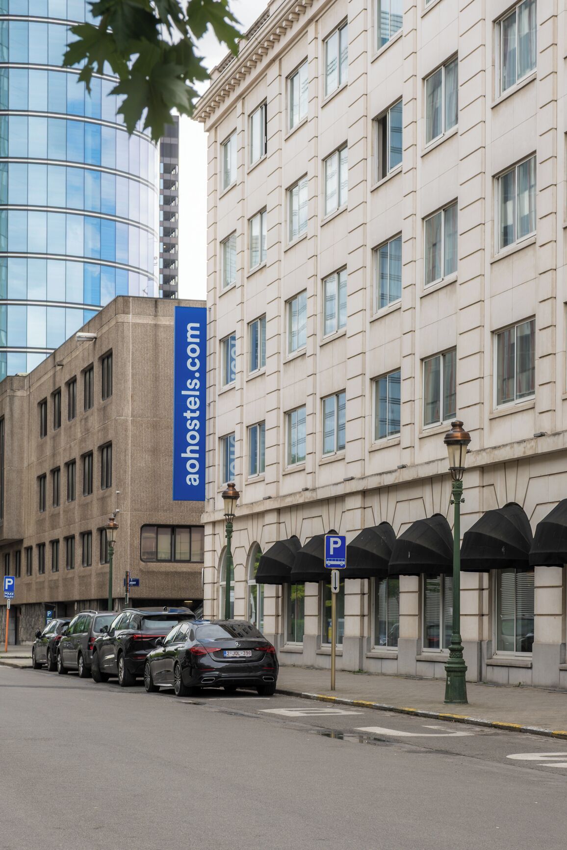 A building with a modern glass facade and a classical facade with multiple windows. There are parking signs and a street lamp visible.