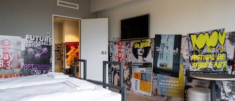Una habitación de hotel moderna con una cama, carteles en las paredes, un televisor y una mesita.