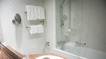 Un baño con ducha de vidrio, un lavamanos y dos toalleros con toallas blancas.