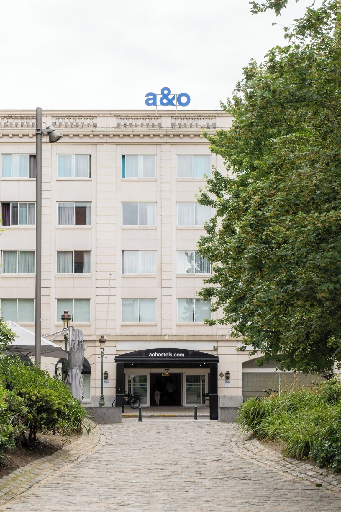 Un edificio con un gran letrero 'a&o', un banner de sitio web 'aohostels.com' y una entrada empedrada.