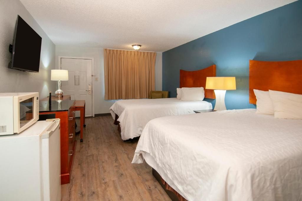 Een hotelkamer met twee bedden, een televisie, een bureau met een lamp en een deur.