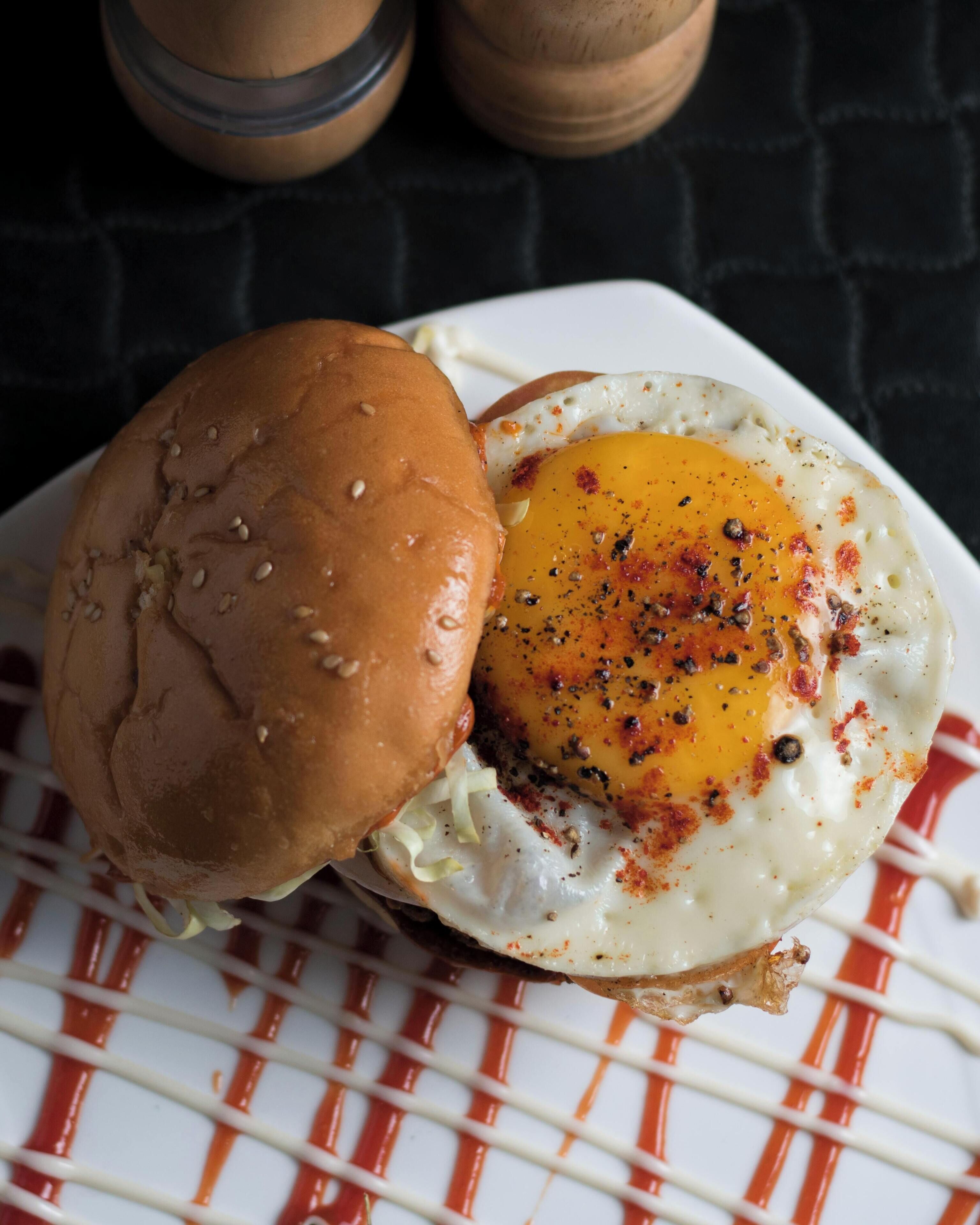 Un sándwich de desayuno con huevo en un pan, servido en un plato blanco con salsa roja.