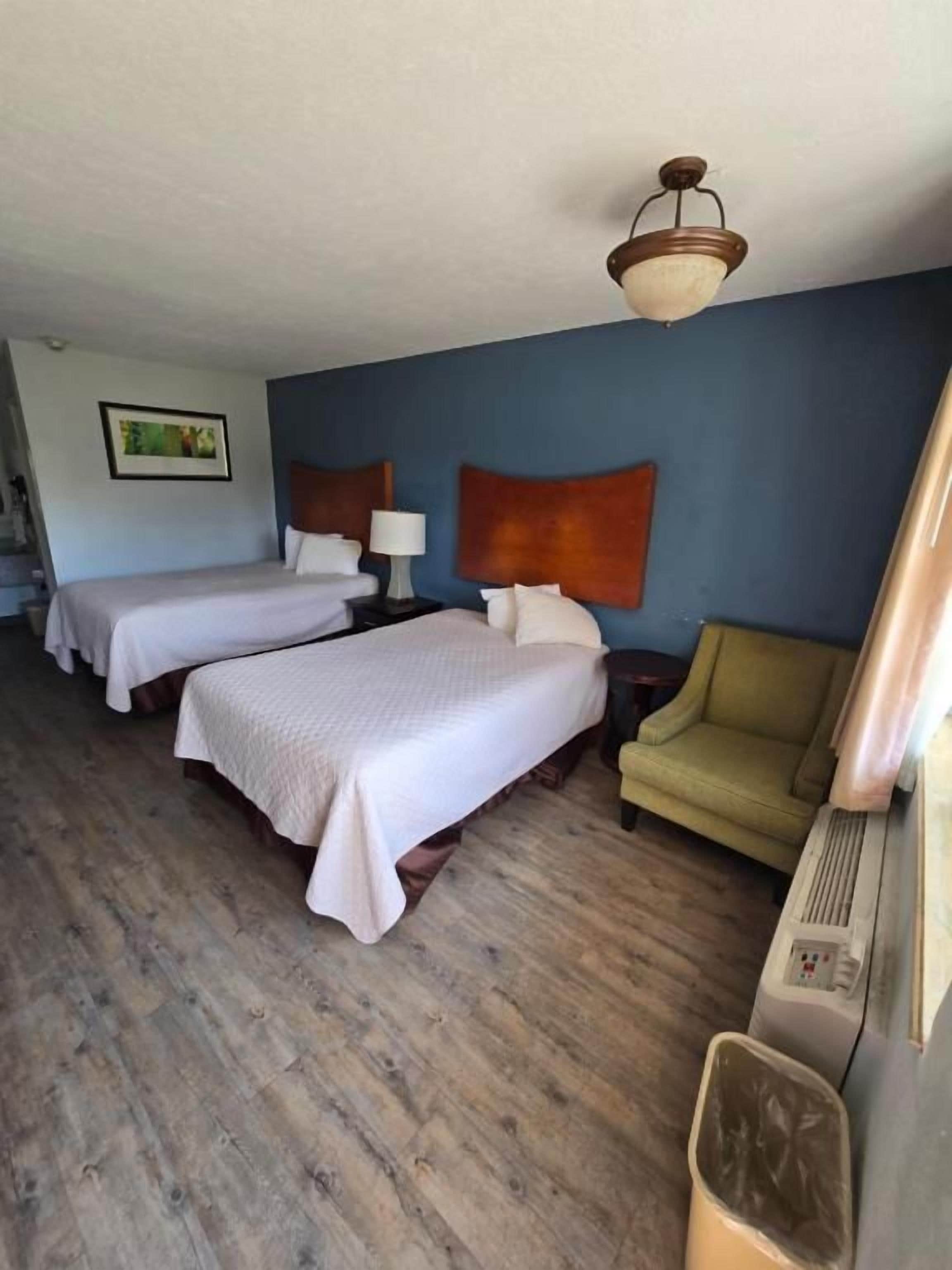 A hotel room with two beds, a sofa, a lamp, and a ceiling light fixture.
