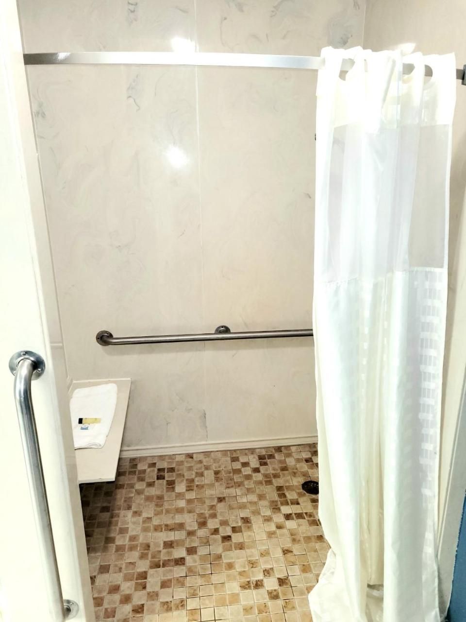 A bathroom with a tiled floor, a handrail, a shower curtain, and a towel rack.