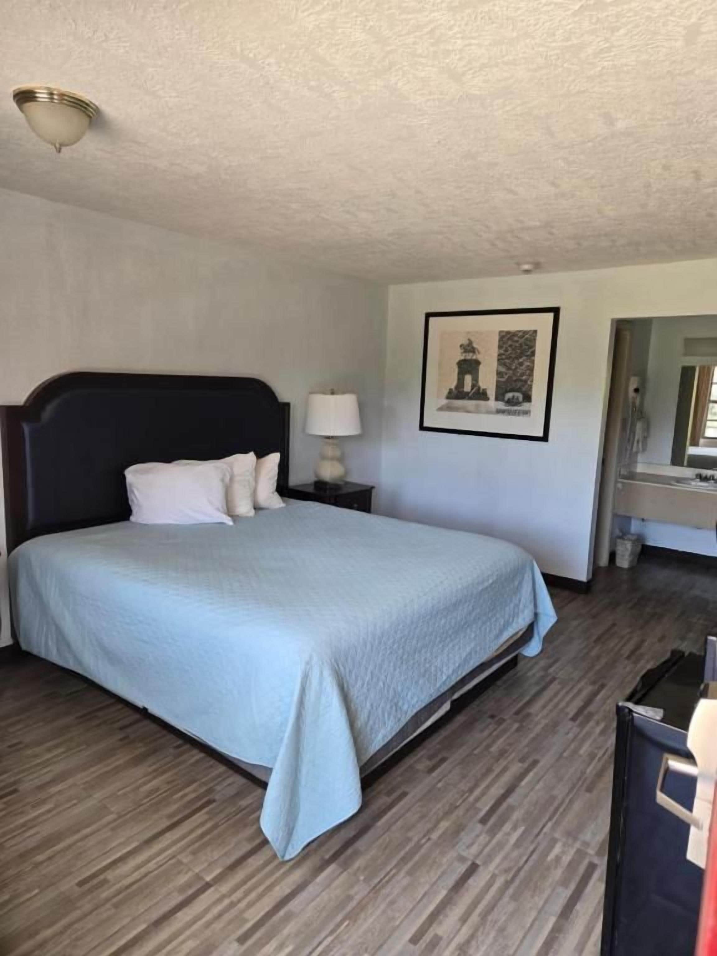 A hotel room with a bed, bedside table, lamp, and a framed picture on the wall.