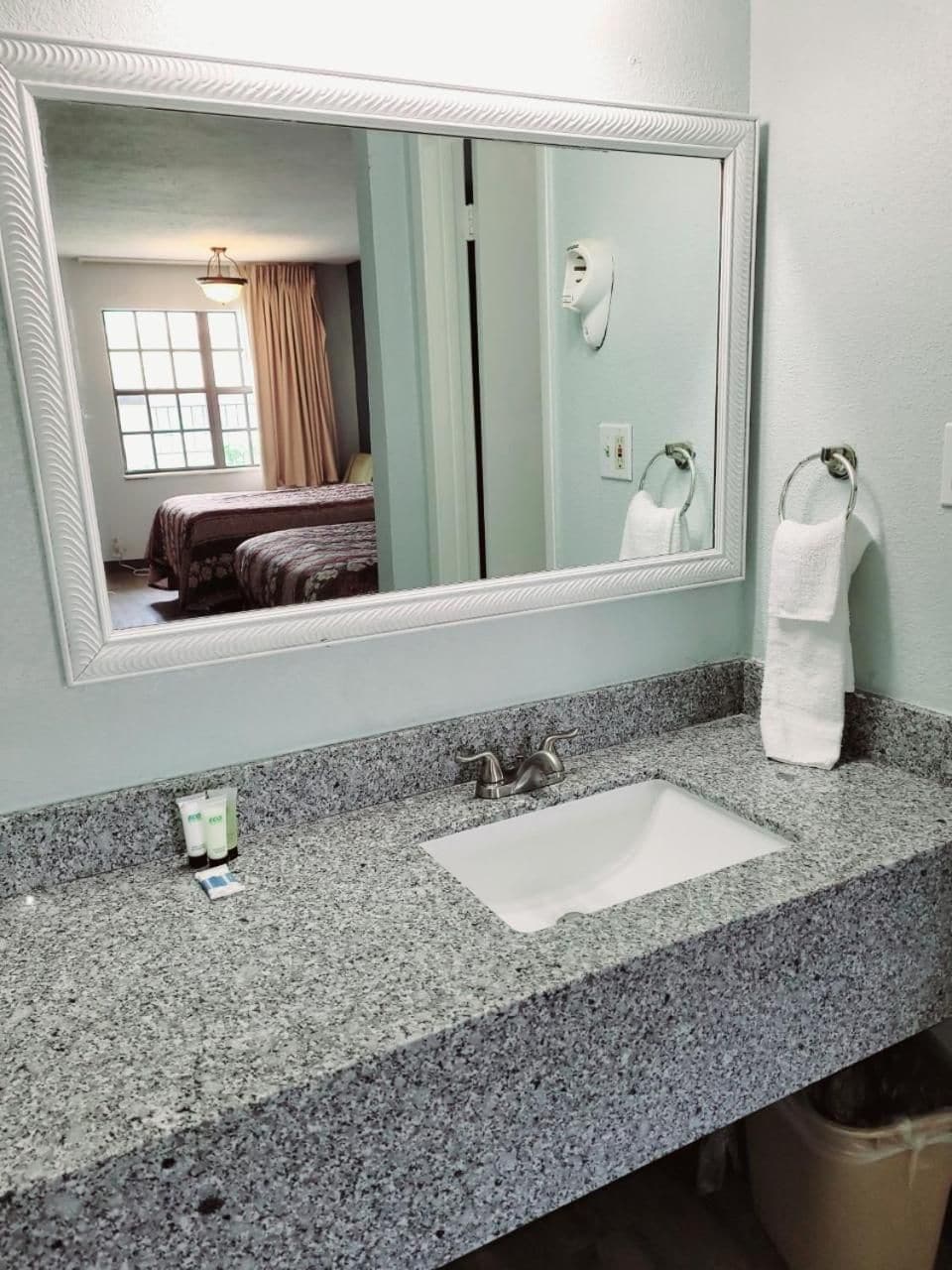 Une salle de bain avec un comptoir en granit, un lavabo blanc, un miroir et un porte-serviettes.
