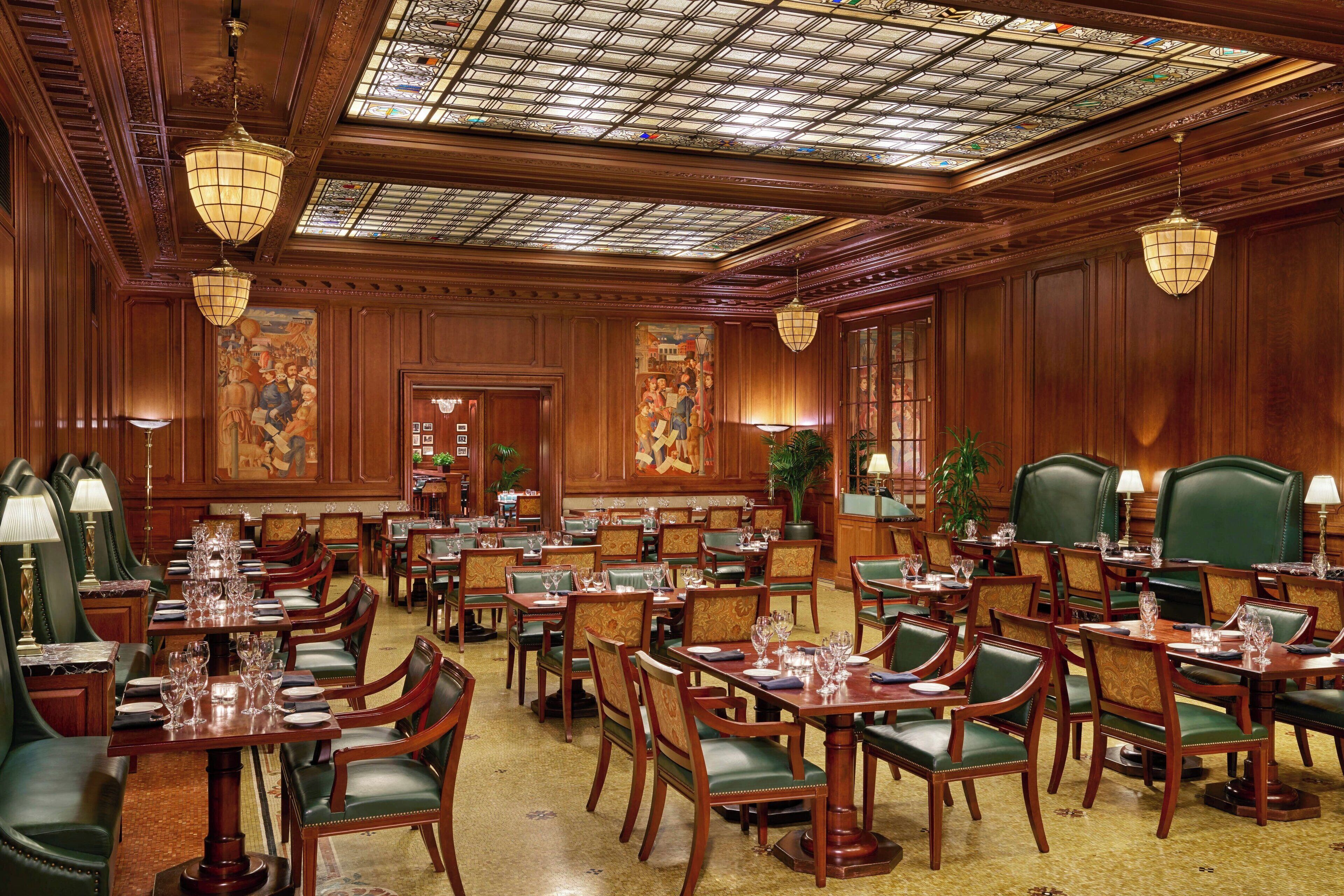 A spacious dining area with multiple tables and chairs, ornate ceiling, and large windows.