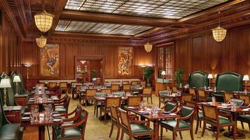 A spacious dining area with multiple tables and chairs, ornate ceiling, and large windows.