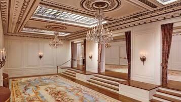 Un salón imponente con techo decorado, candelabros, una alfombra grande y una escalera.