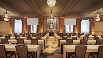 A conference room with rows of tables and chairs, large chandeliers, and ornate wall decorations.