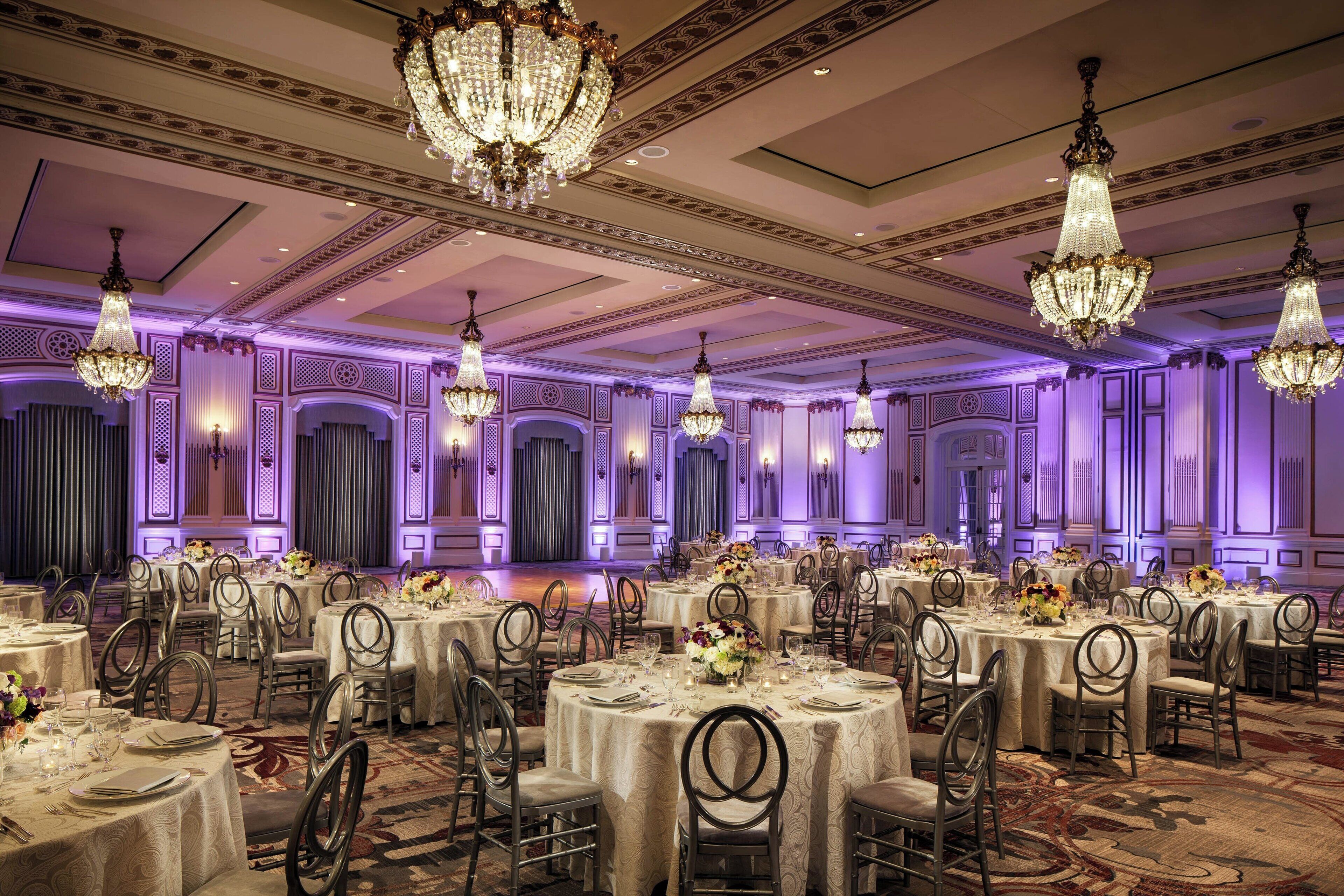 A banquet hall with round tables, chairs, and chandeliers.