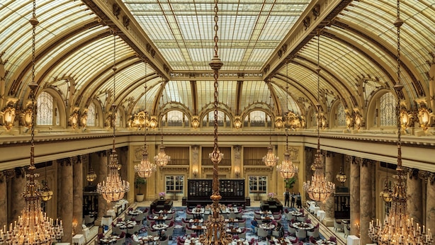 A grand hall with a high arched ceiling and chandeliers, featuring multiple dining tables and chairs arranged for service. - Palace Hotel, a Luxury Collection Hotel, San Francisco (San Francisco)