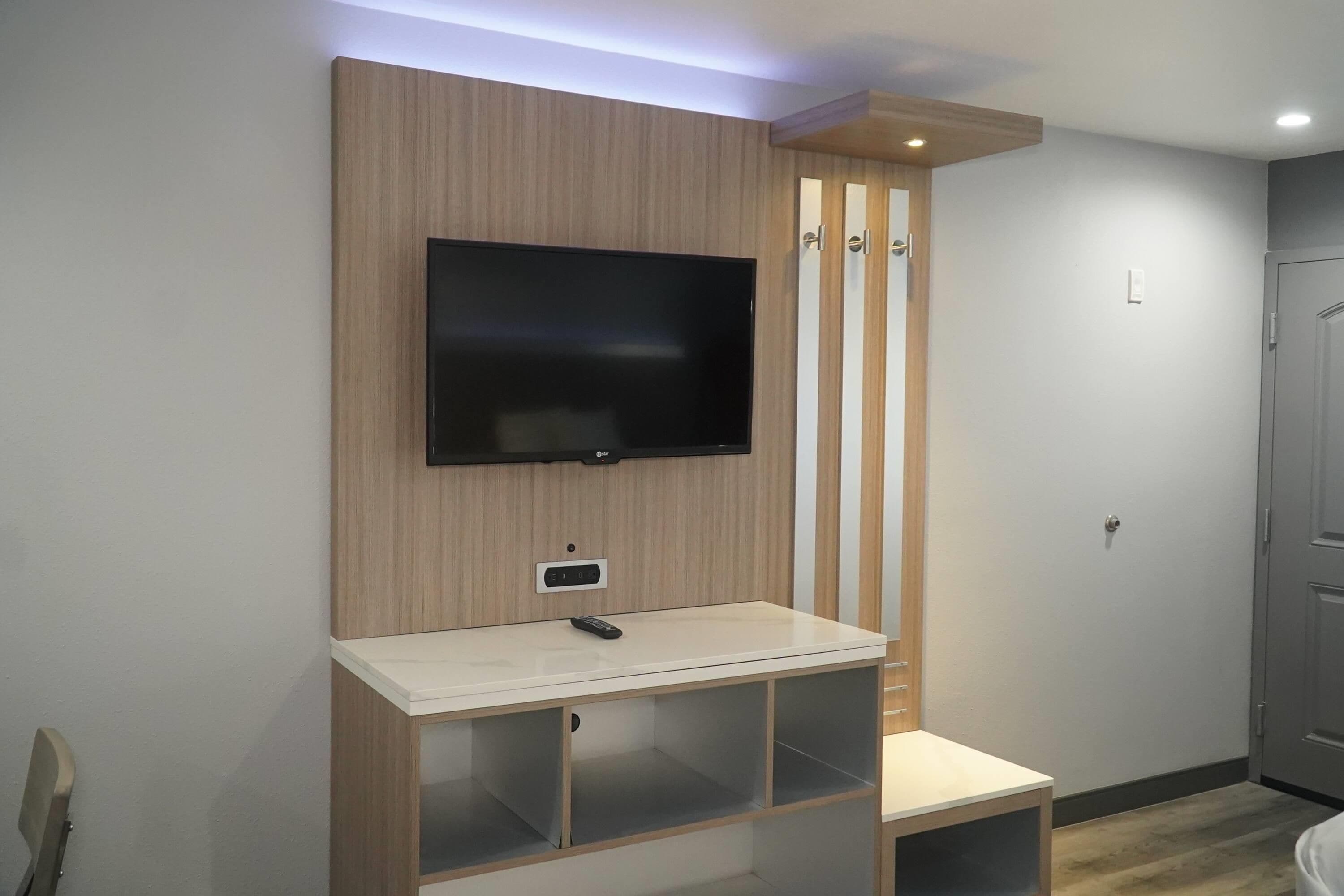 A modern room with a mounted TV, a small desk with storage, and a wardrobe.