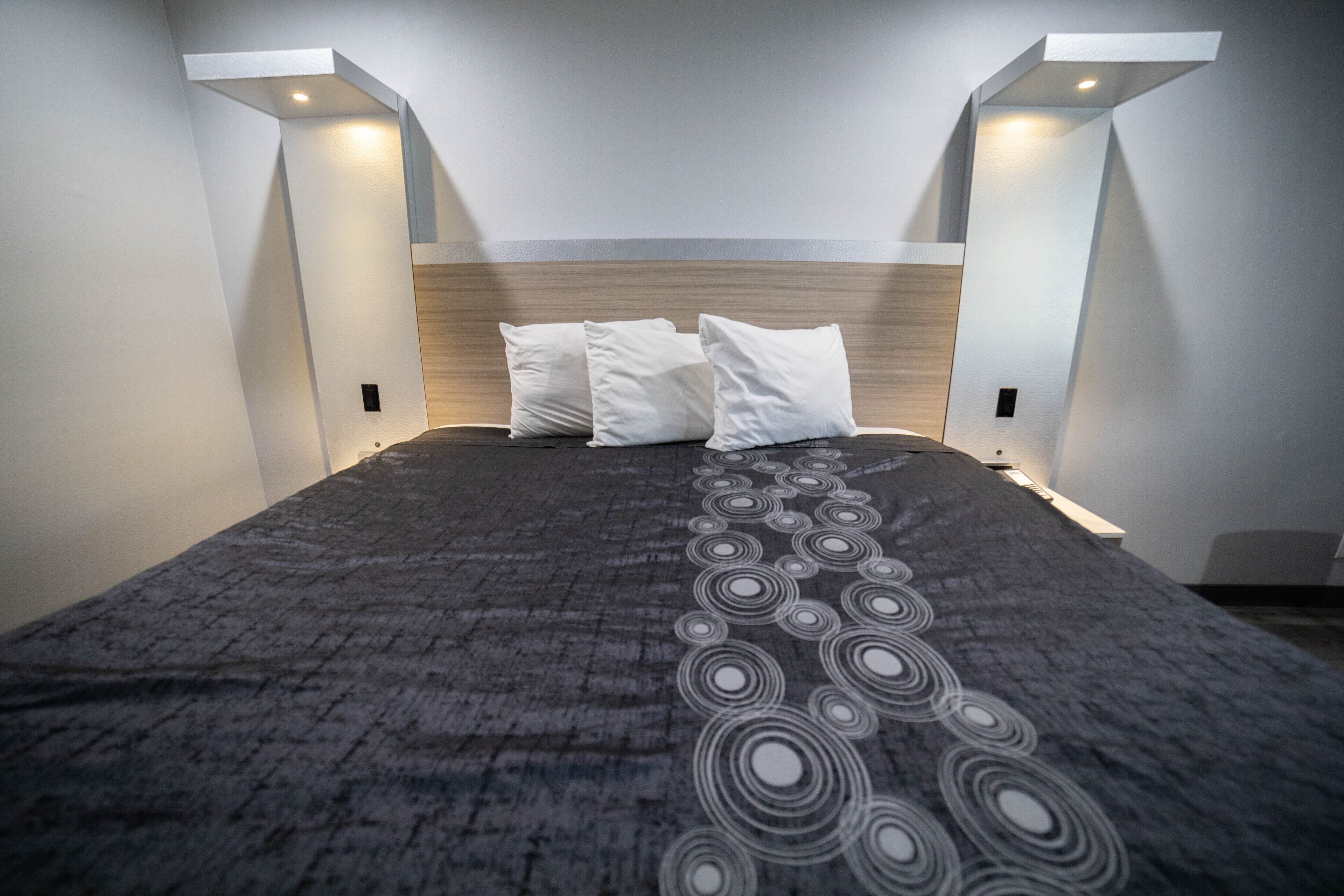A modern bedroom with a large bed, a wooden headboard, and two wall-mounted light fixtures.