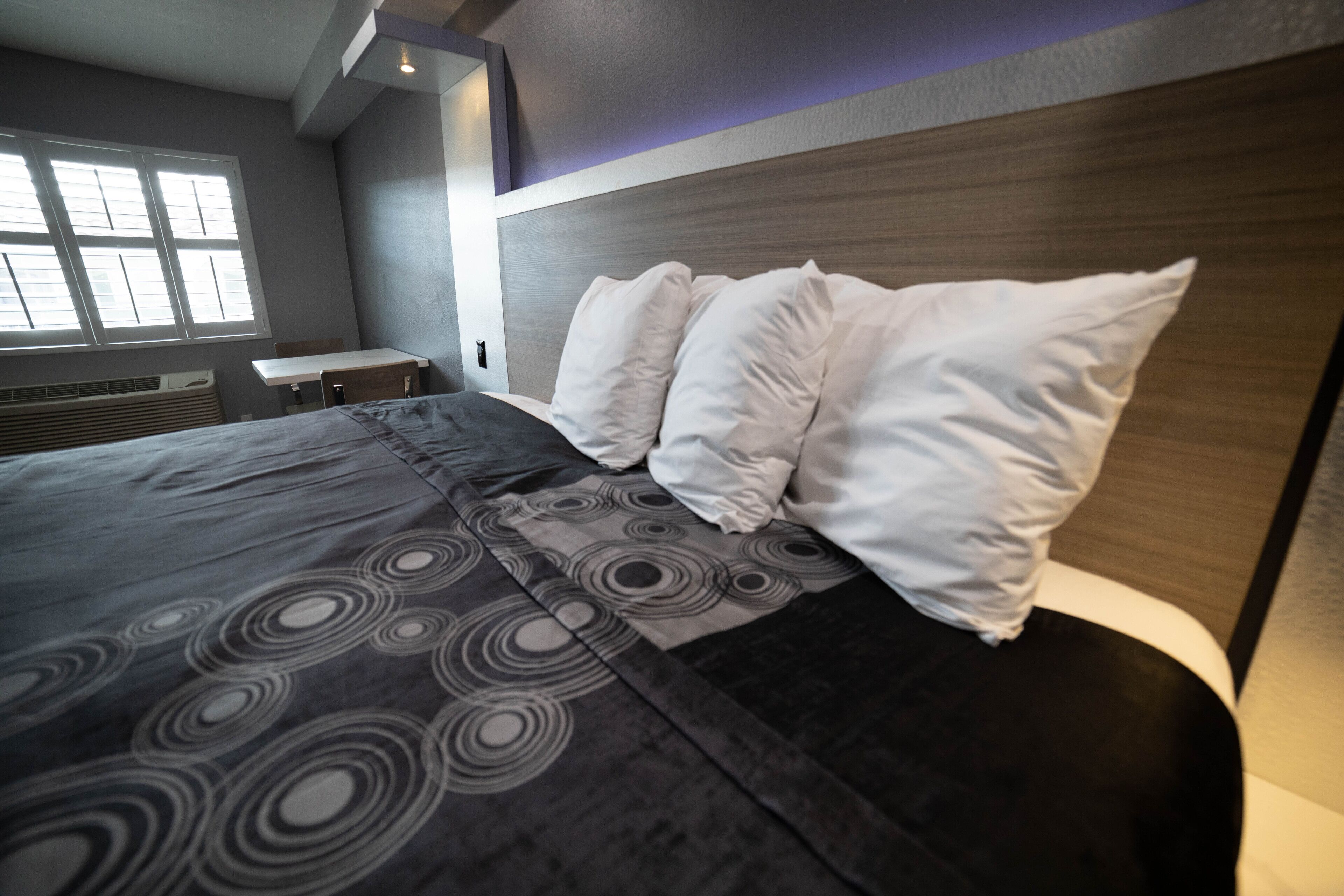 A modern hotel room with a large bed, a wooden headboard, and a window with blinds.