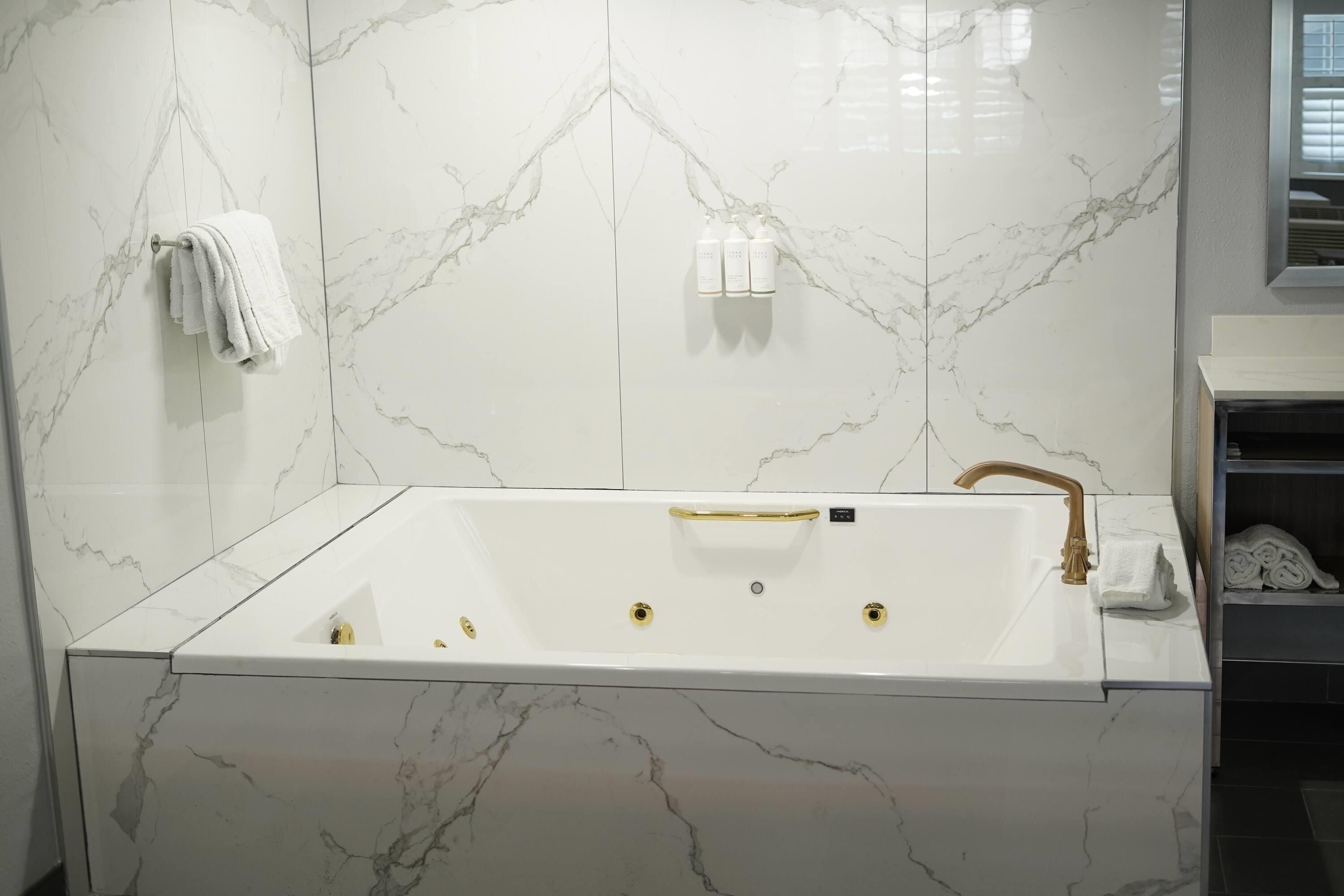 A modern bathroom with a marble vanity, a bathtub with gold fixtures, and a towel rack.
