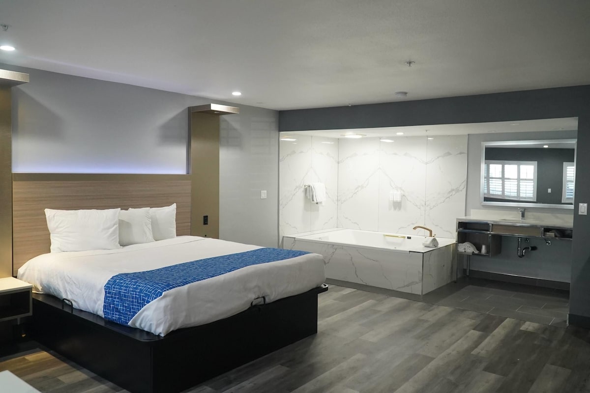 Une chambre d’hôtel moderne dotée d’un grand lit, d’une salle de bain séparée avec baignoire et d’une coiffeuse avec miroir.