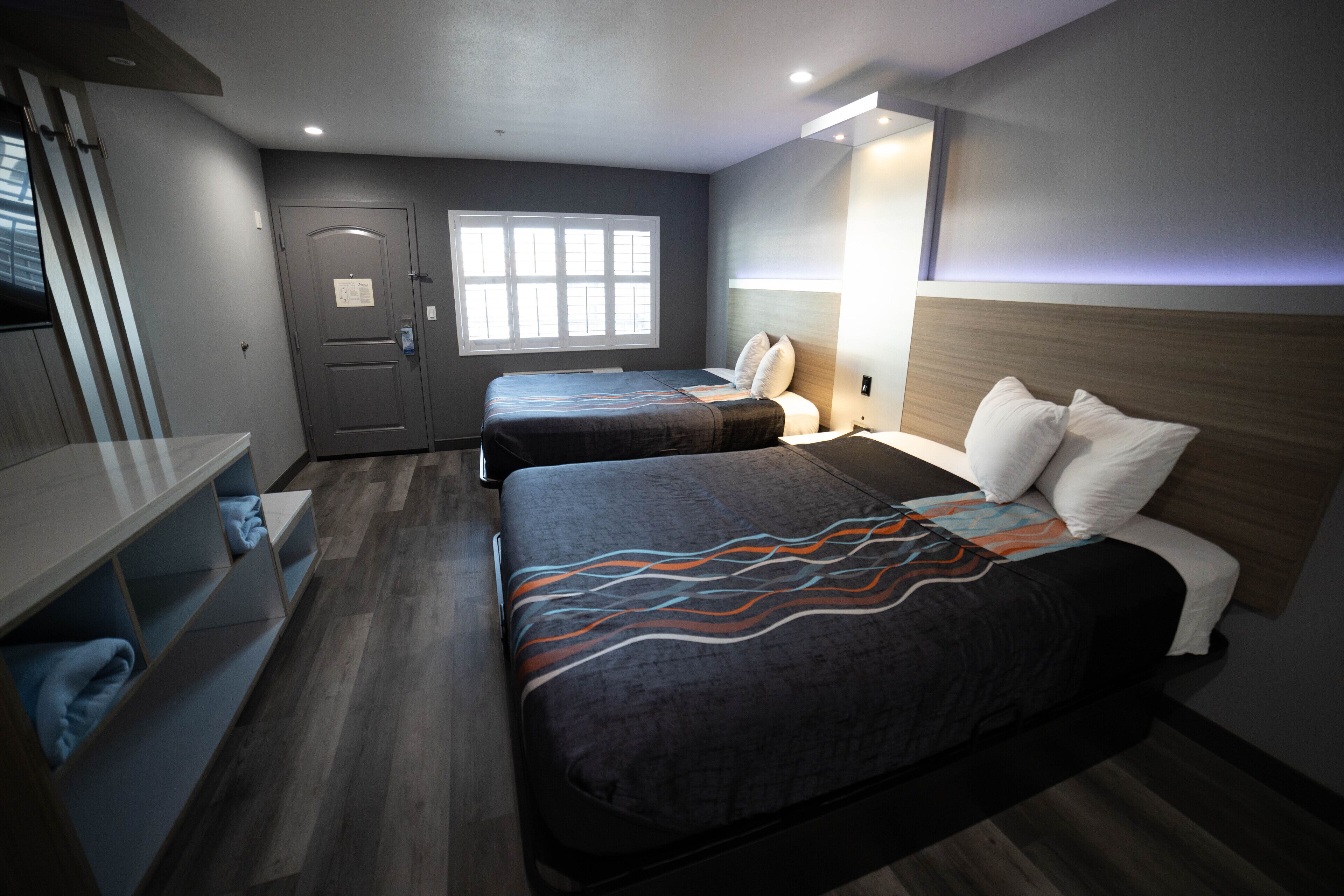 A hotel room with two beds, a desk, and a window.