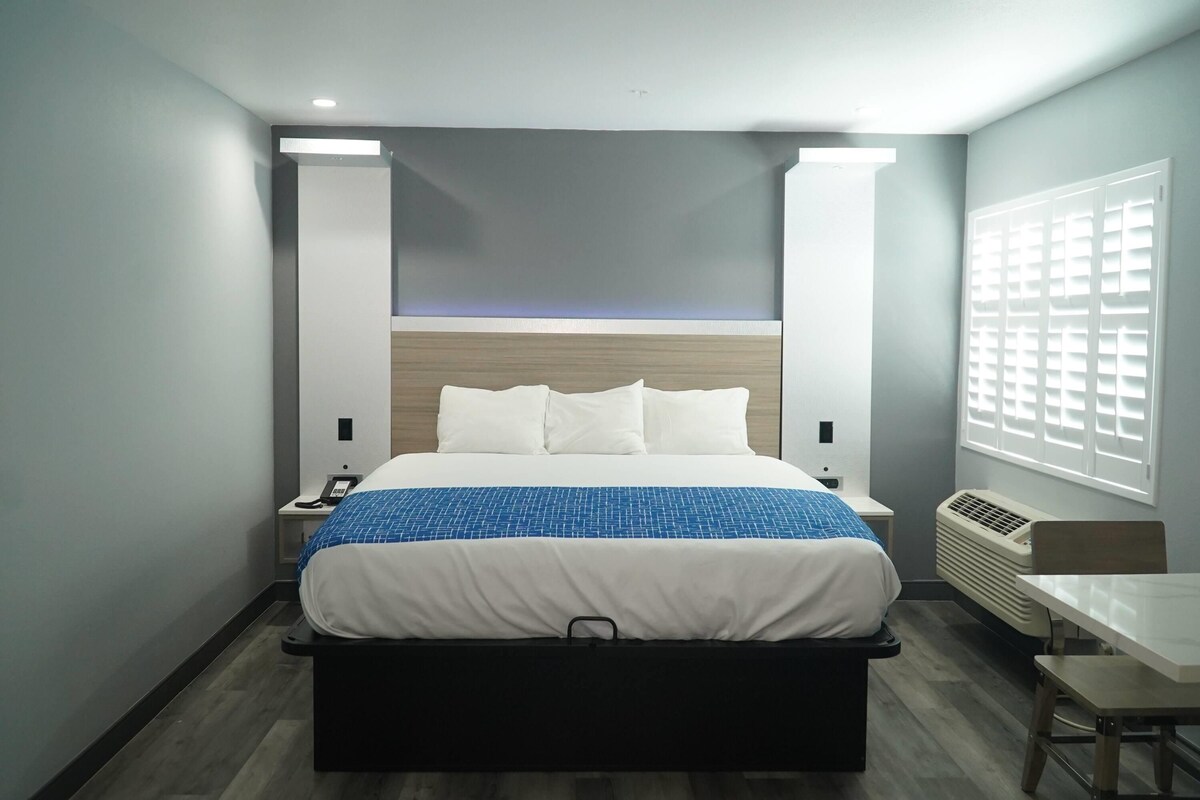 Une chambre d’hôtel avec un lit, des tables de chevet, un bureau et une fenêtre avec des stores.