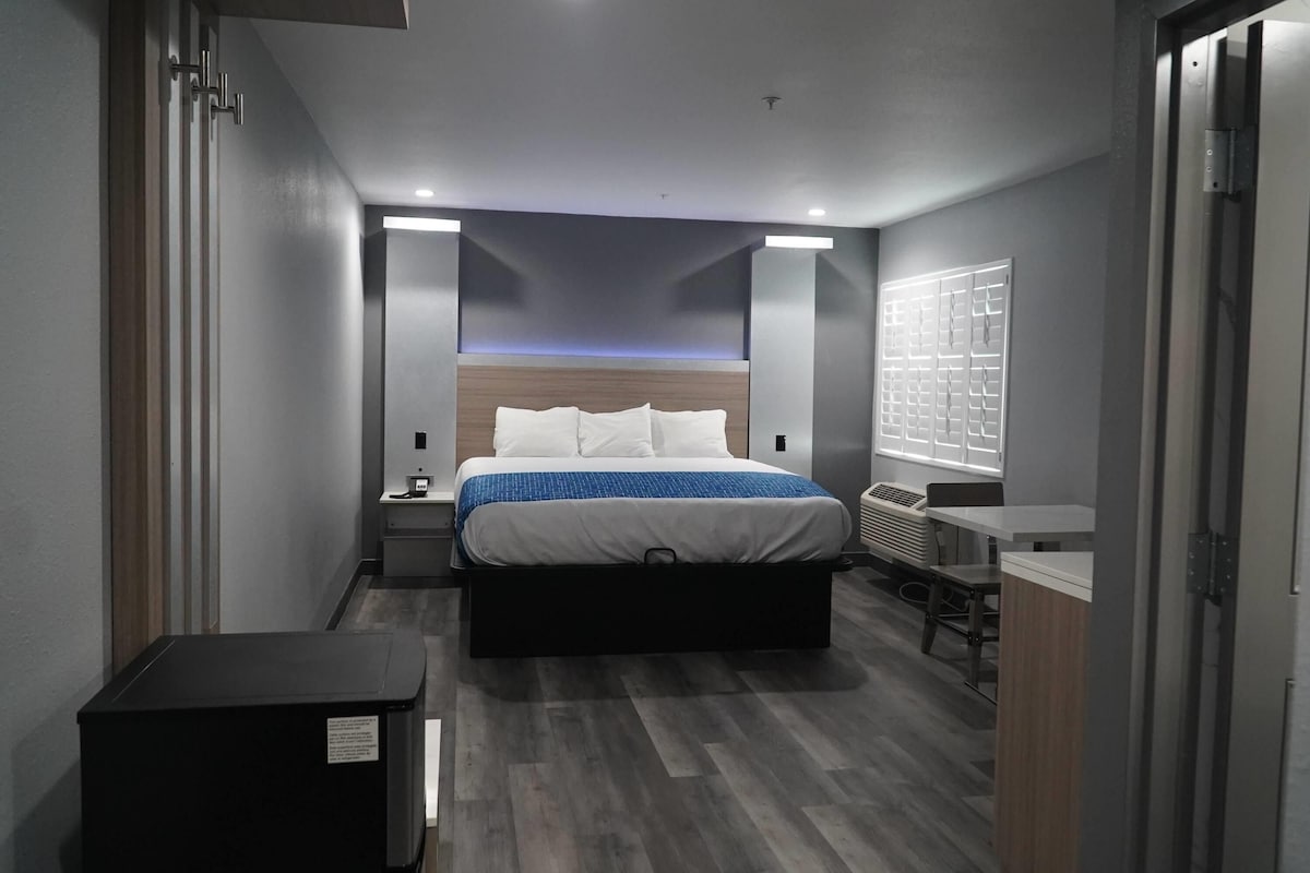Une chambre d’hôtel moderne équipée d’un lit, de tables de chevet, d’un bureau et d’une fenêtre avec des stores.